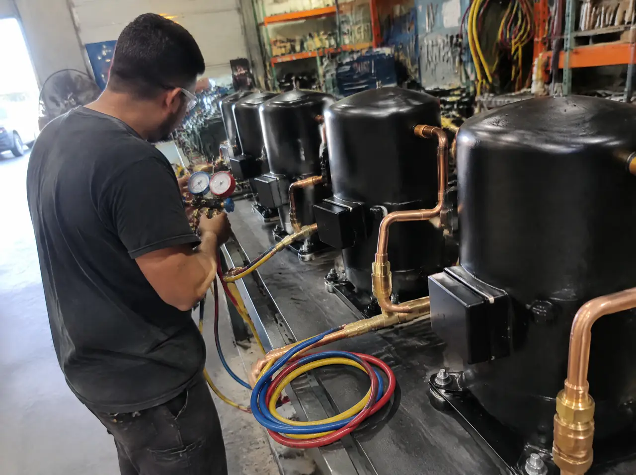 Technician with a gauge set beside a row of plain black chiller casings