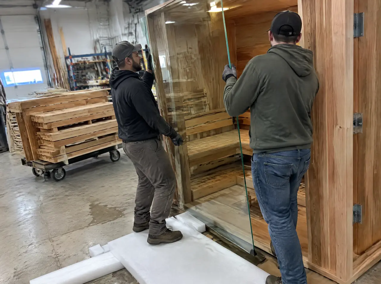 Two workers fitting a toughened-glass panel into a test-assembled cedar frame